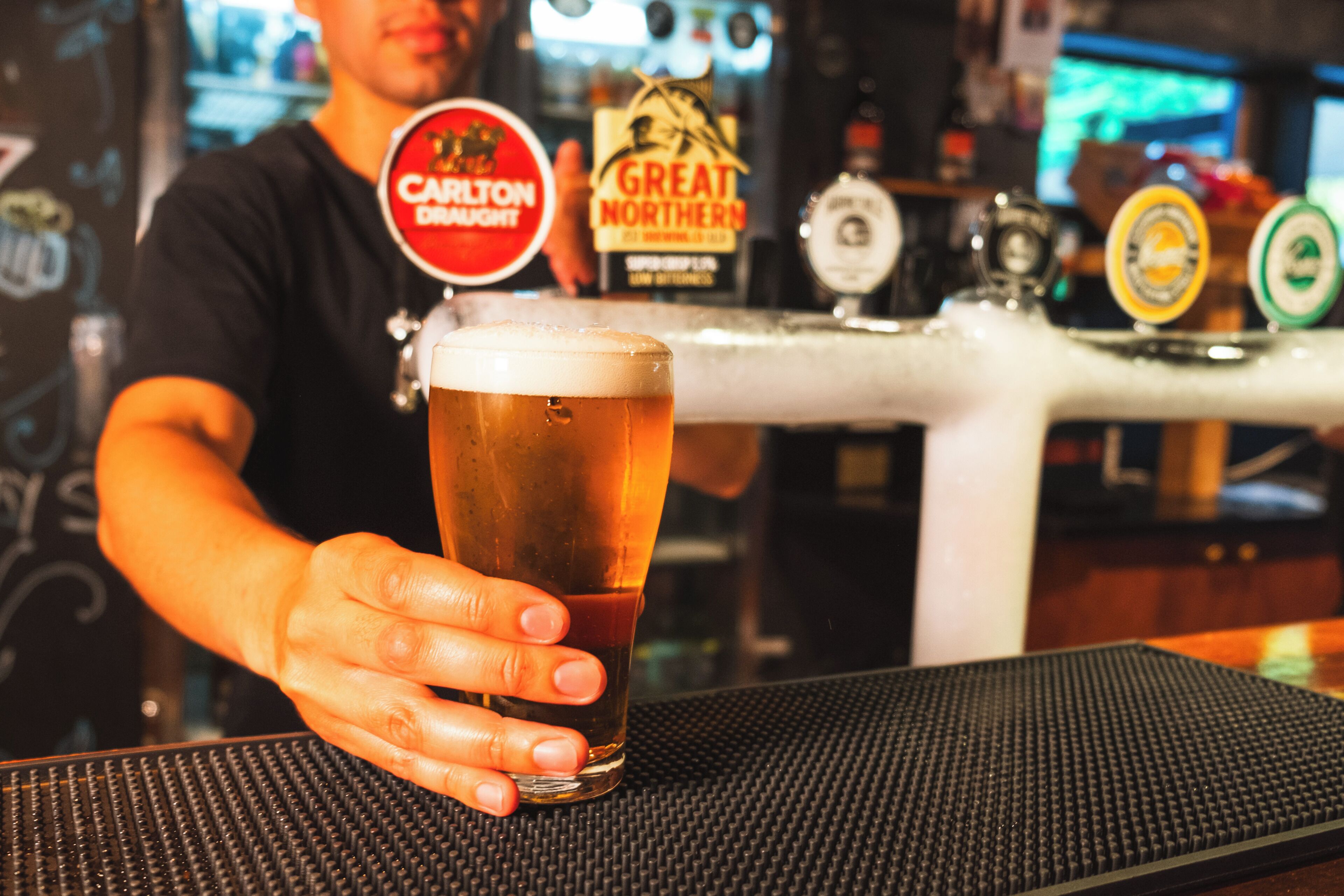 Un barman tenant un verre de bière, avec une tireuse en arrière-plan.