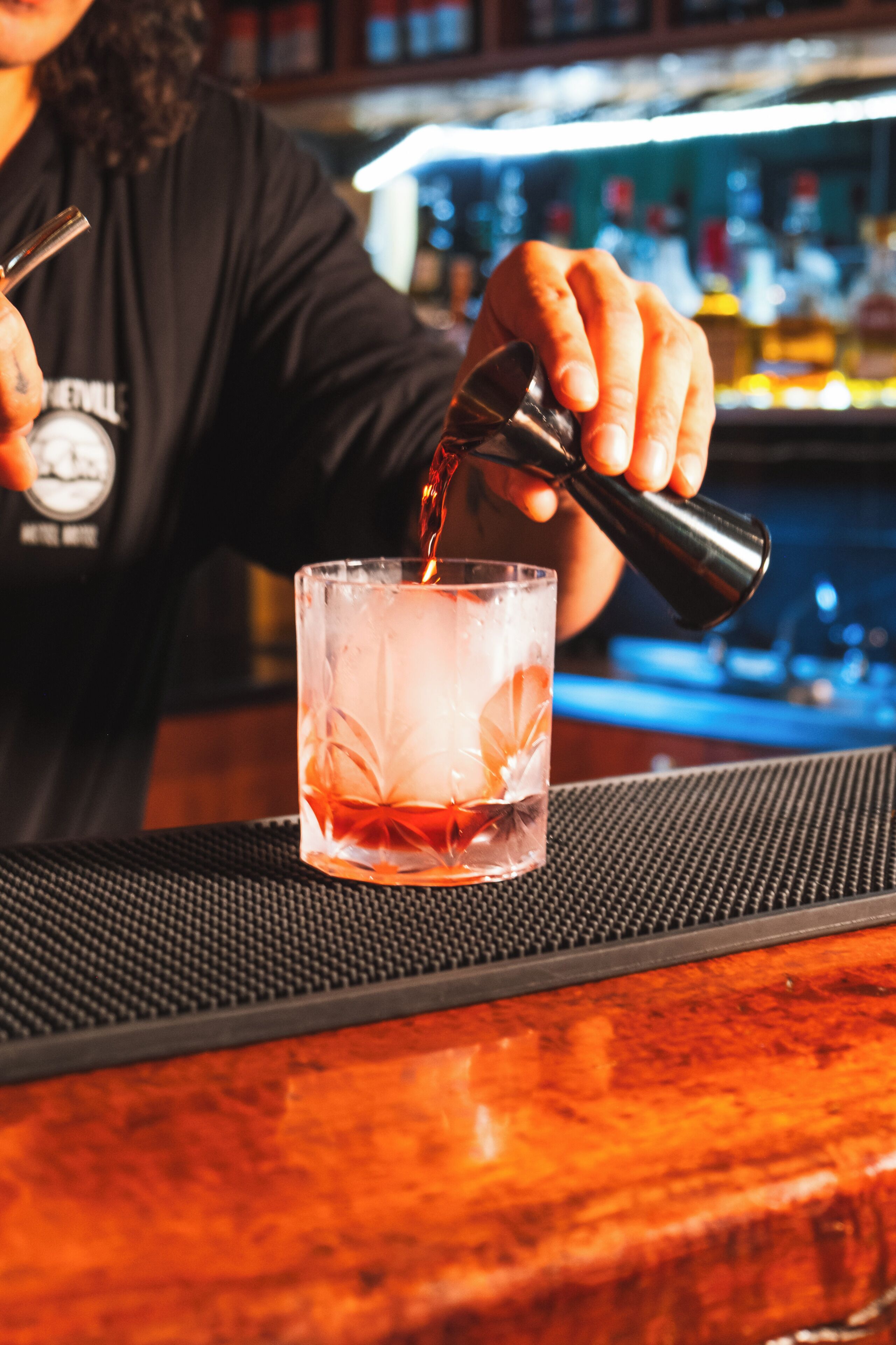 A bartender pouring a drink into a glass with a floral pattern.
