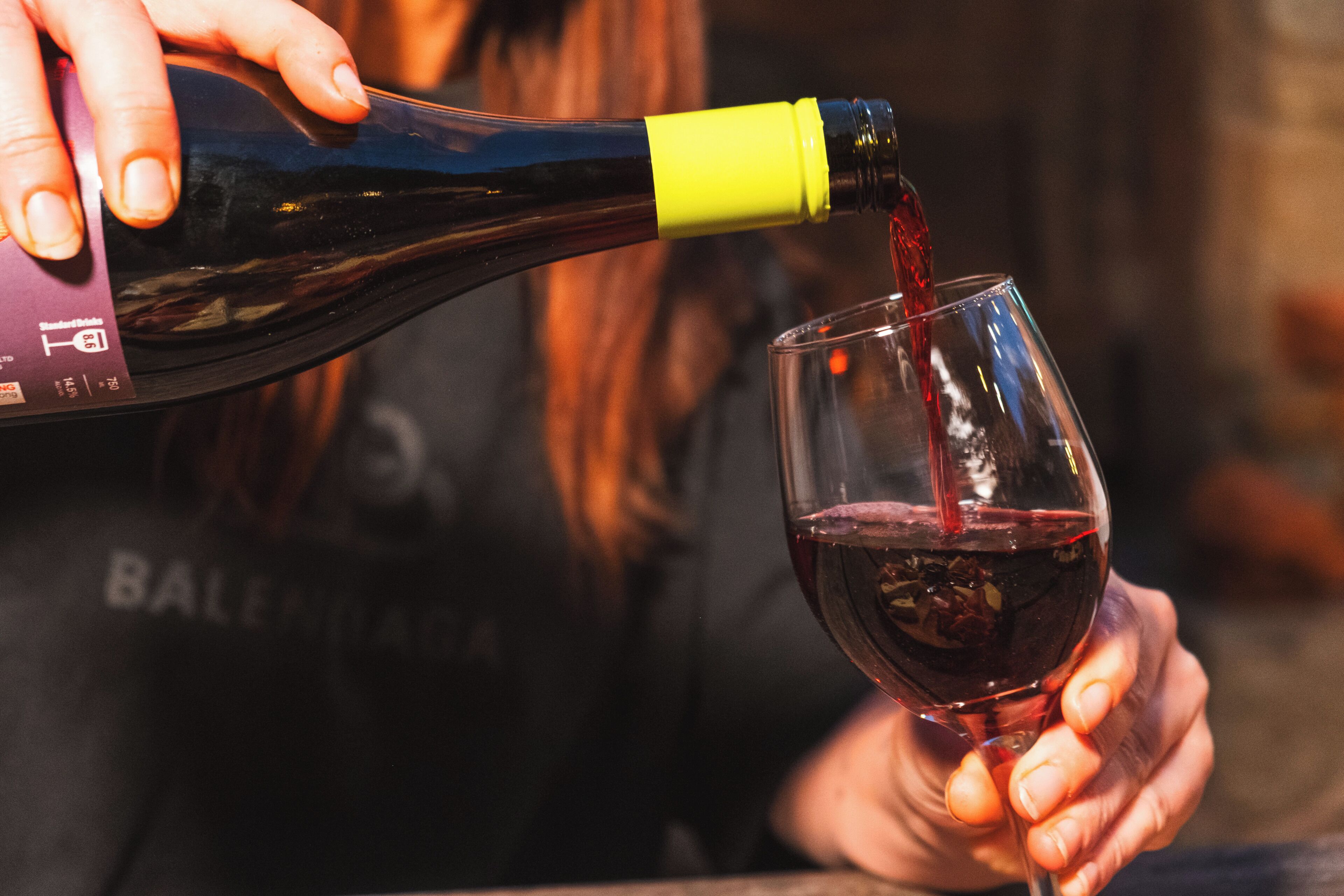 A person pouring red wine from a bottle into a glass.