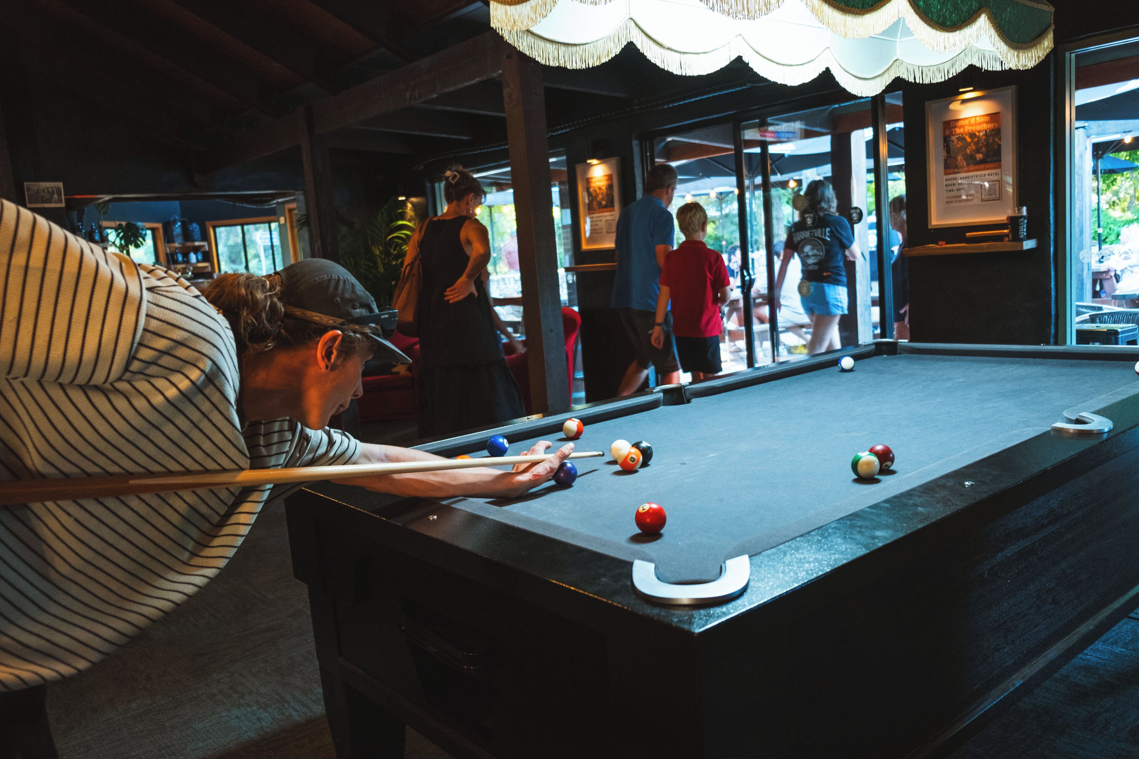 A pool table with balls, a person playing, and a view of the outside through a glass door.