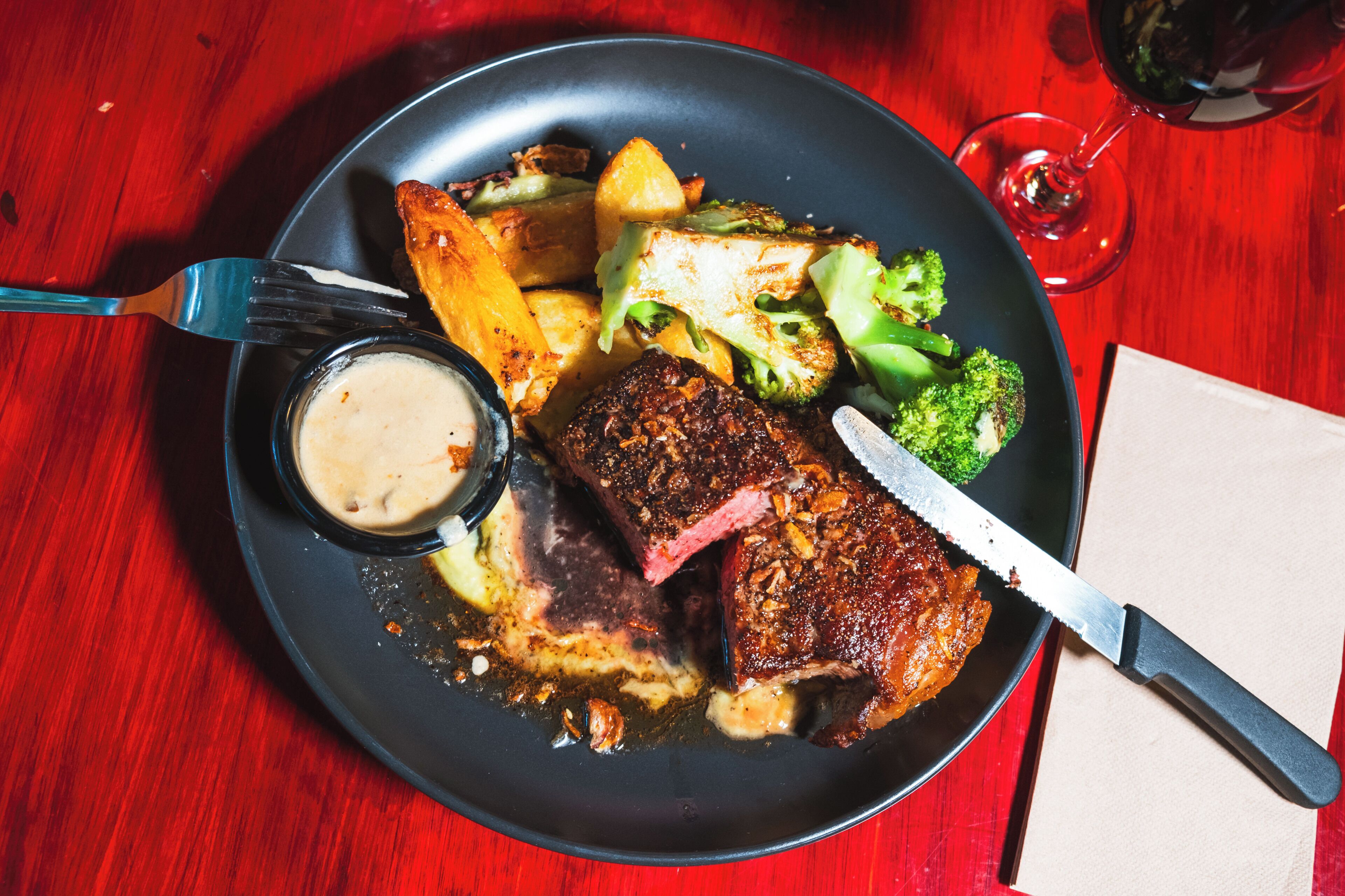 A plate with steak, potatoes, and broccoli on a red table.