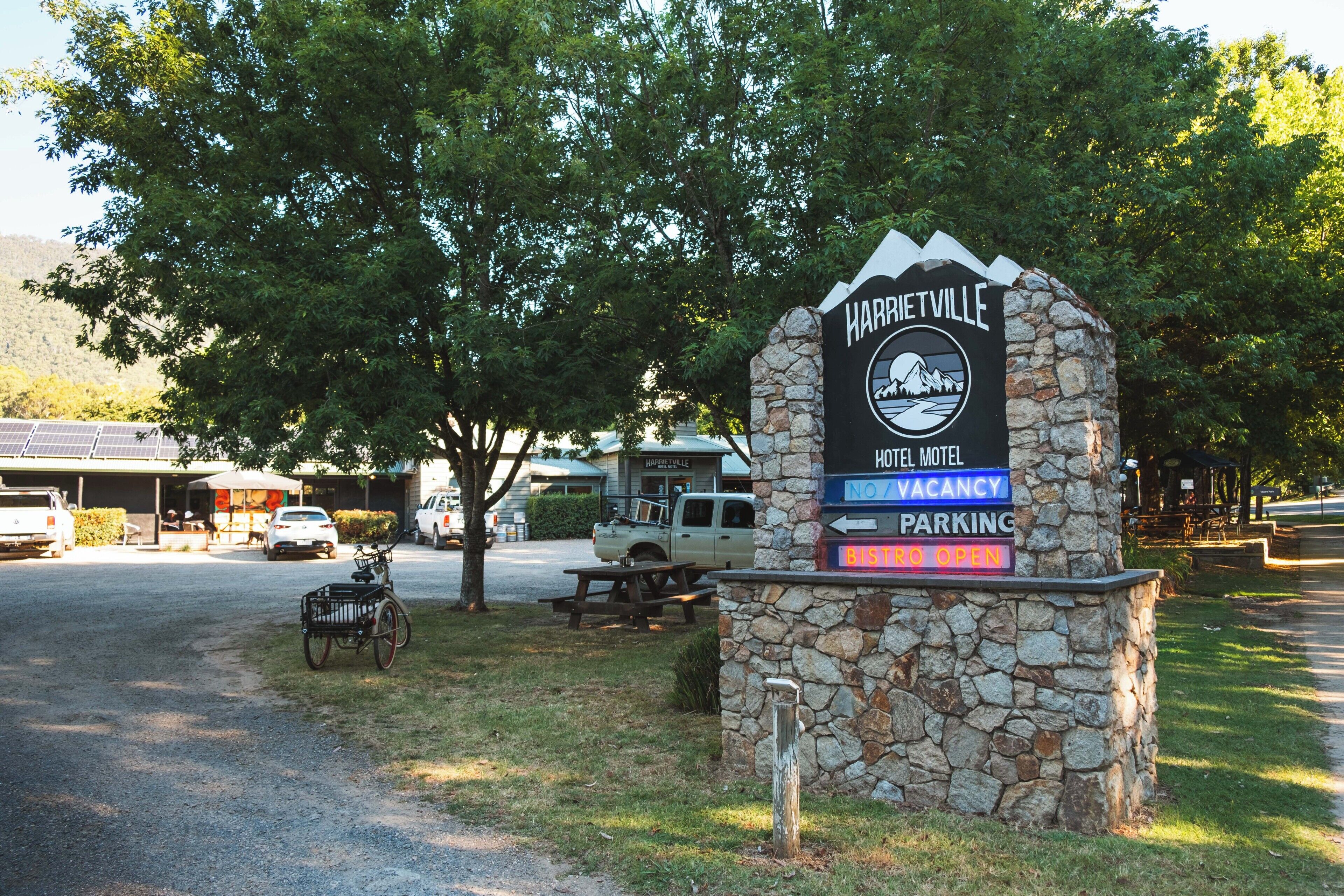 A stone sign with 'Harrisonville Hotel Motel' and 'No Vacancy' signs, a bicycle, and a picnic table.