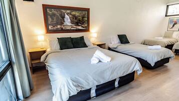 A hotel room with two beds, a painting of a waterfall, and a window with curtains.