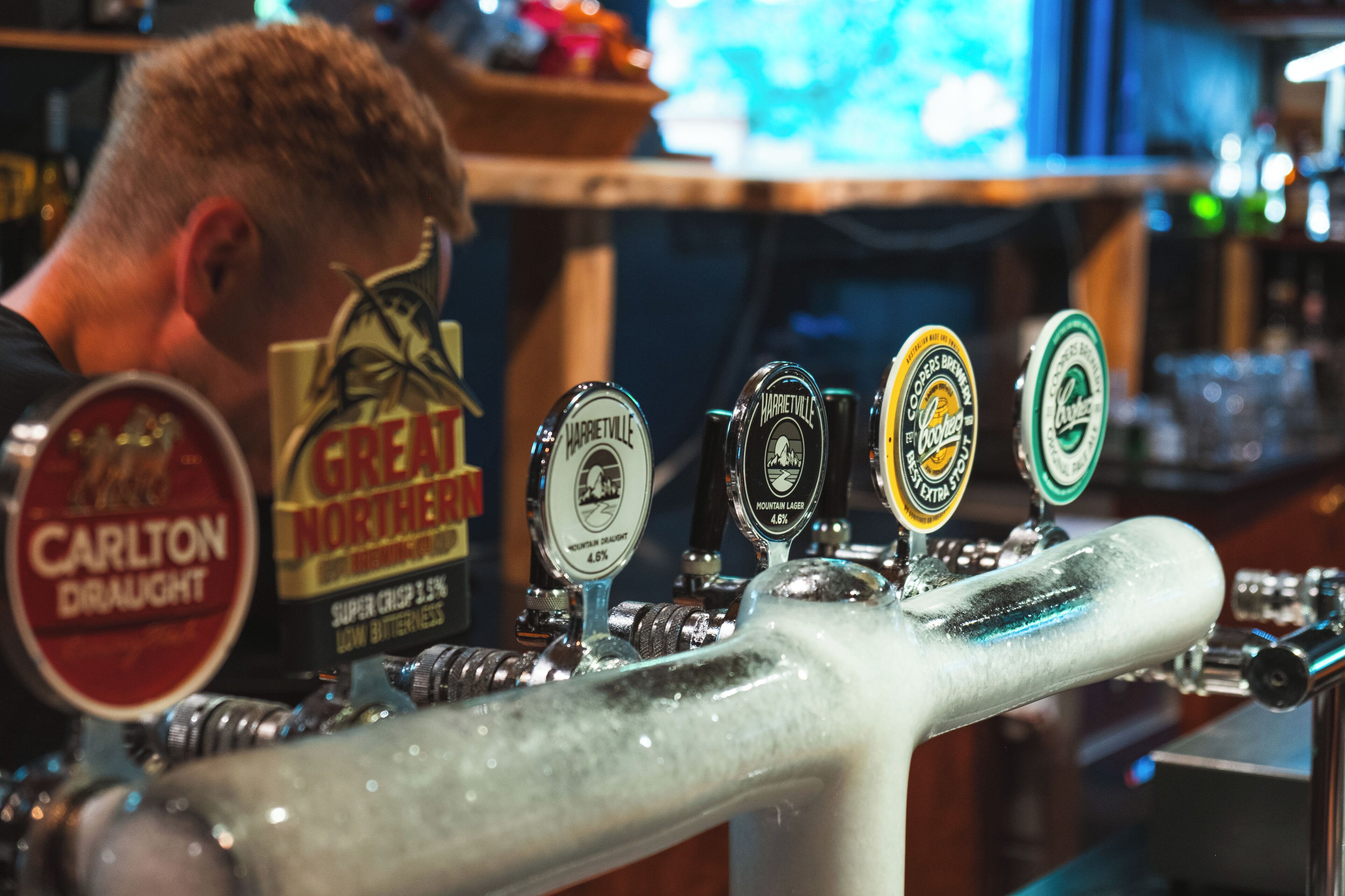 Una llave de grifo de bar con varias etiquetas de cerveza, incluyendo 'Carlton Draught' y 'Great Northern'.