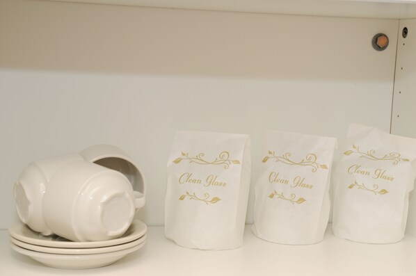 A stack of white ceramic mugs and plates with decorative gold text on a white shelf. - The Peninsula Motor Inn (Tyabb)