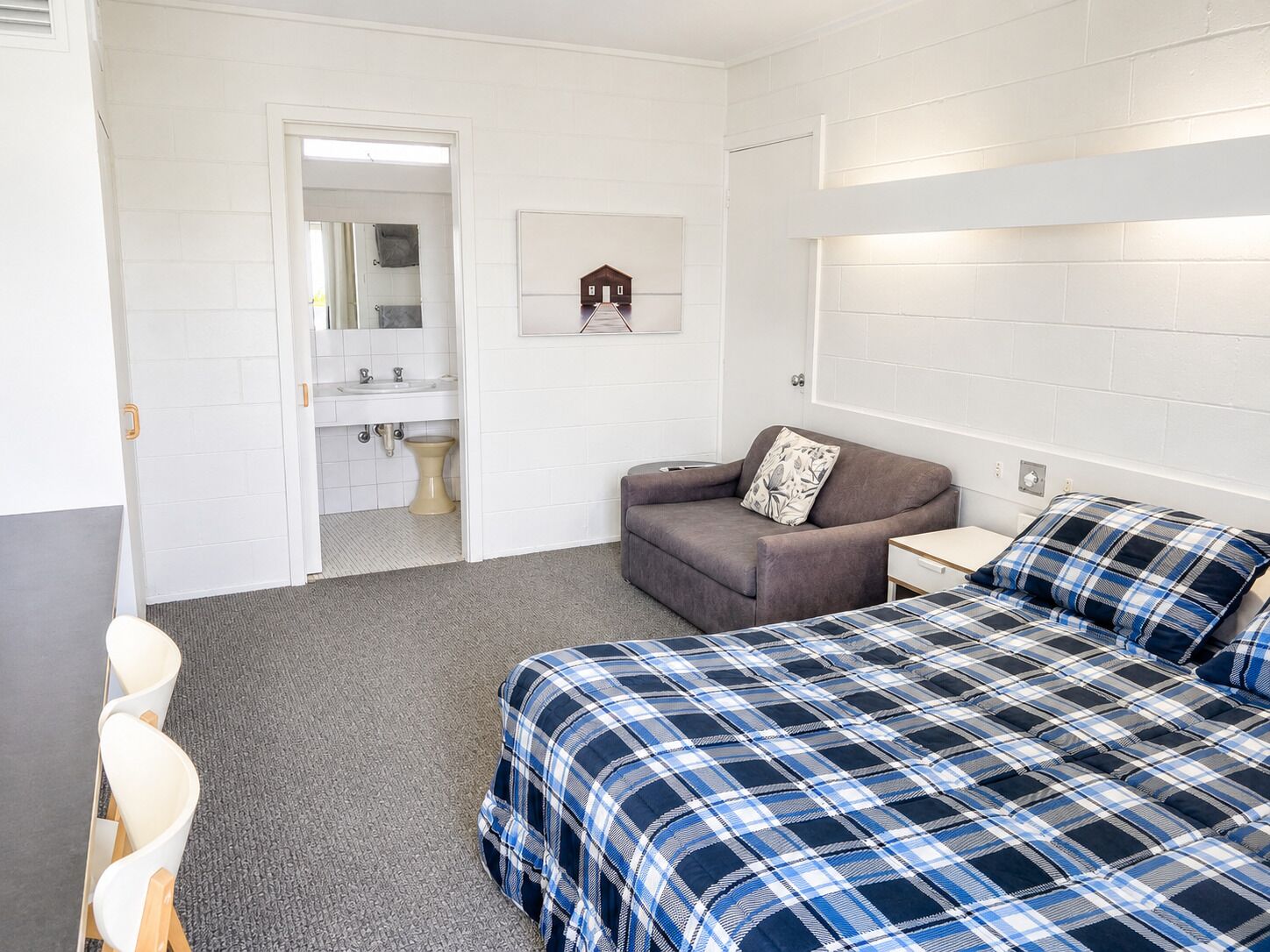 A room with a bed, a sofa, a small table, a chair, and a bathroom visible through an open door.