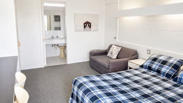 A room with a bed, a sofa, a small table, a chair, and a bathroom visible through an open door.