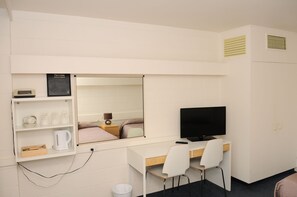 Una habitación de hotel con escritorio, silla, televisor, estante con artículos de aseo y espejo.