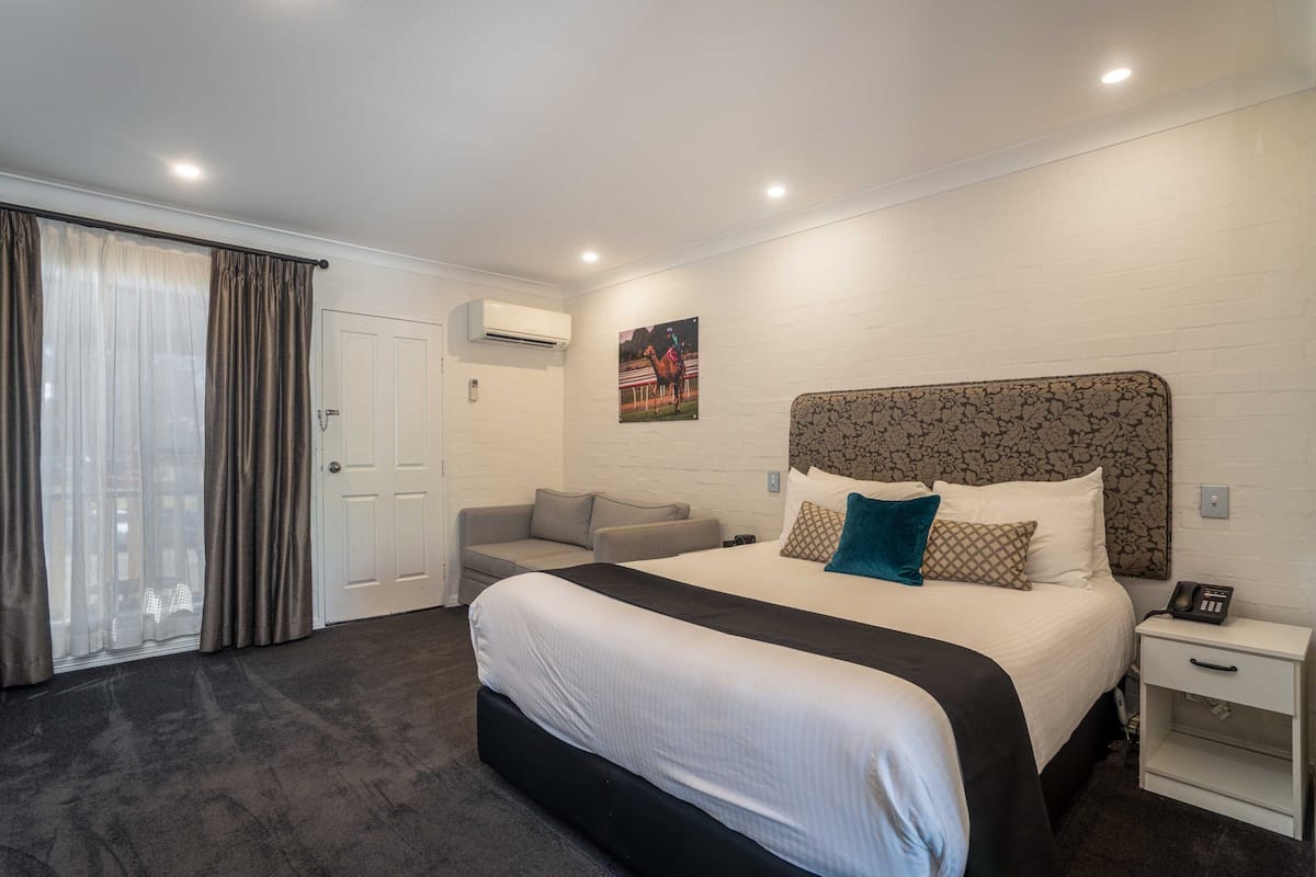 Habitación de hotel con una cama grande, un sofá, una mesita pequeña y un aire acondicionado instalado en la pared.