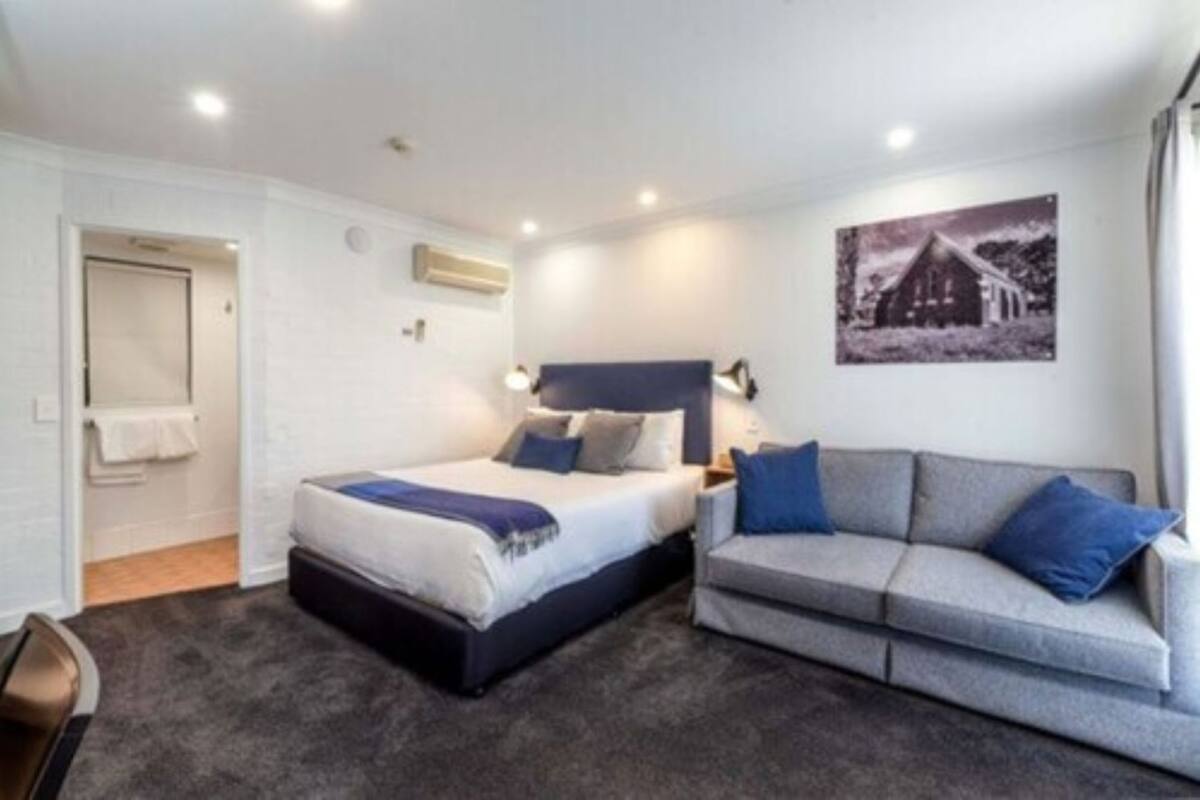 Un dormitorio con cama, un sofá gris, aire acondicionado de pared y un cuadro enmarcado.