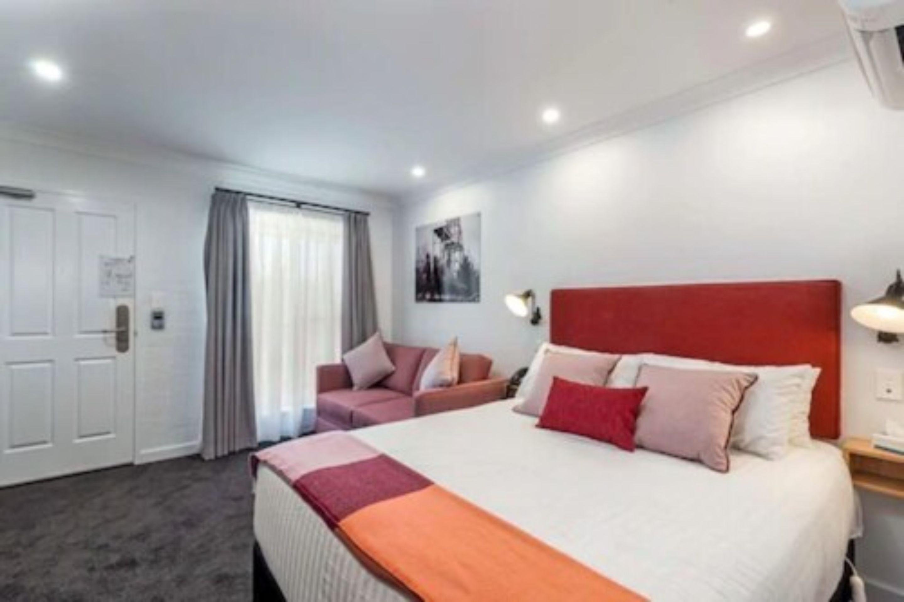 A hotel room with a large bed, a sofa, a desk, and a window with curtains.