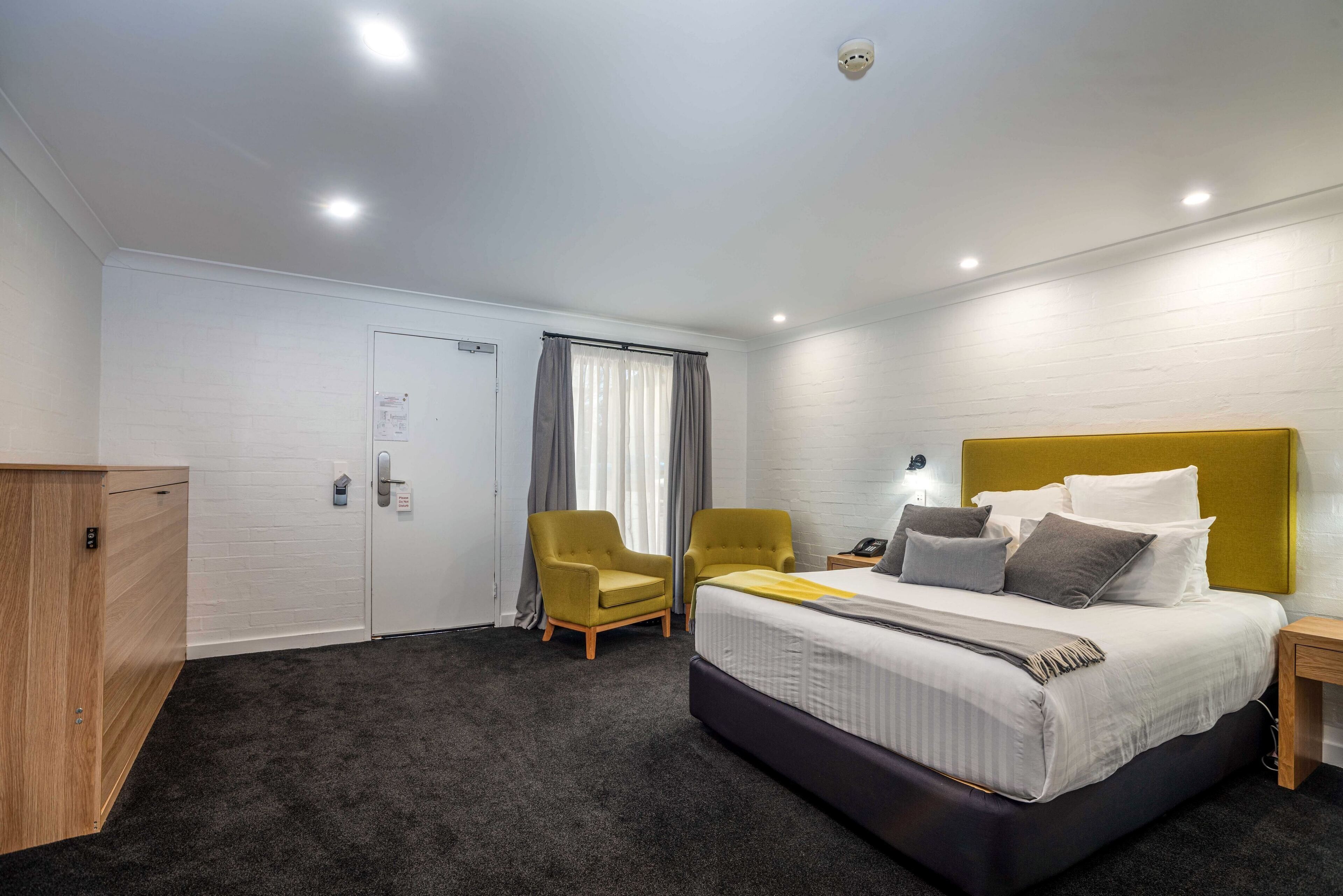 Ein Hotelzimmer mit einem Bett, zwei Sesseln, einem Schreibtisch, einem Kleiderschrank und einer Tür.