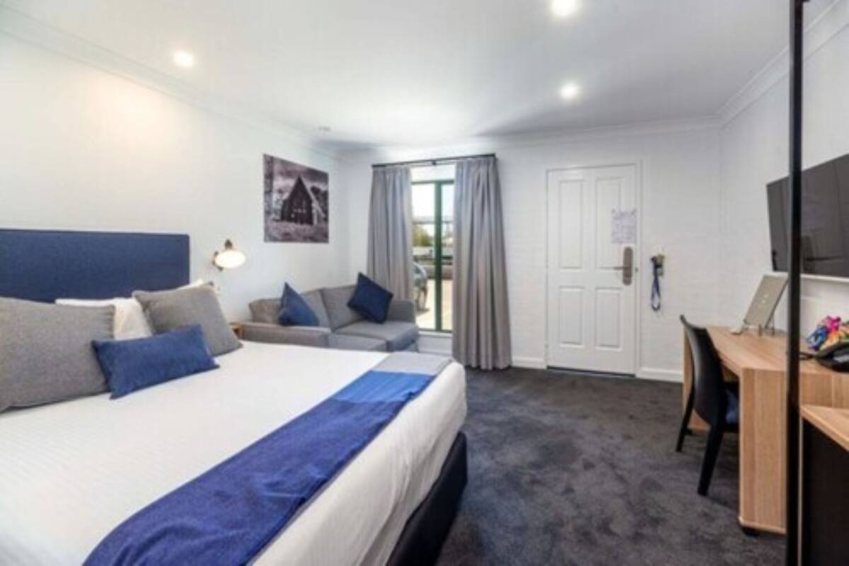 Una habitación de hotel con cama, escritorio, silla, sofá y televisión.