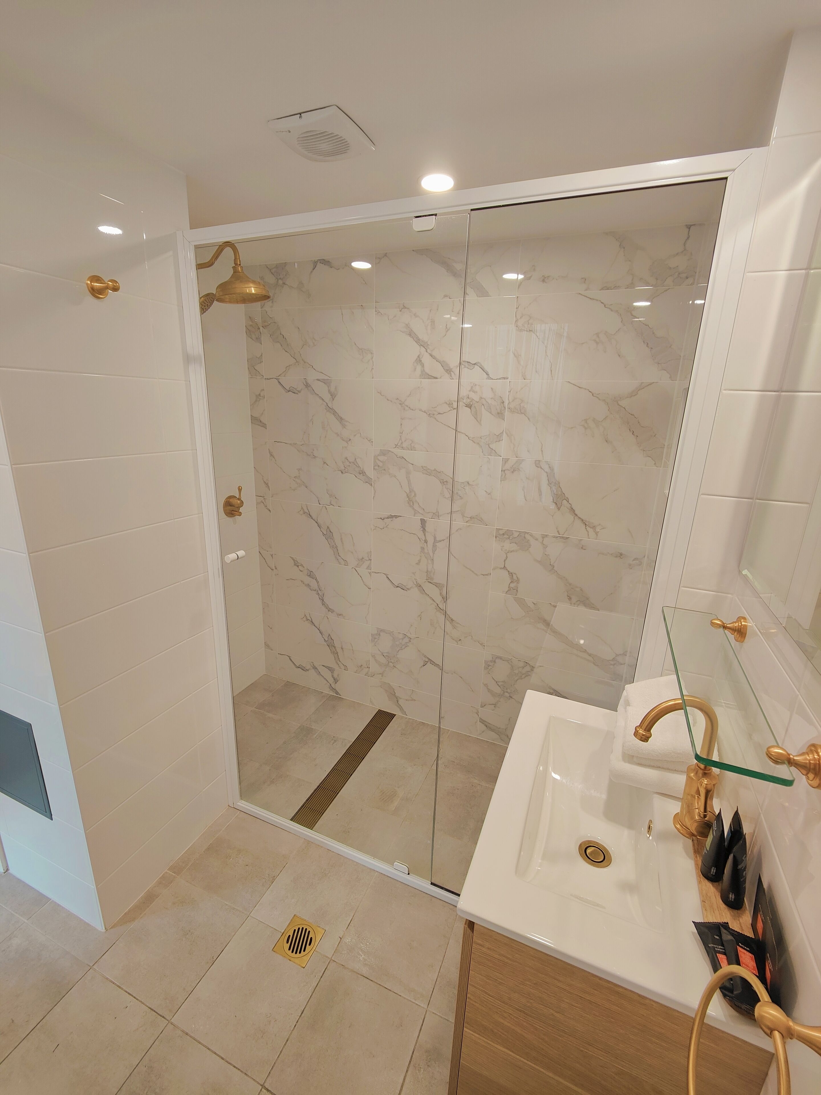 Un baño moderno con ducha de vidrio, baldosas de mármol y detalles dorados.