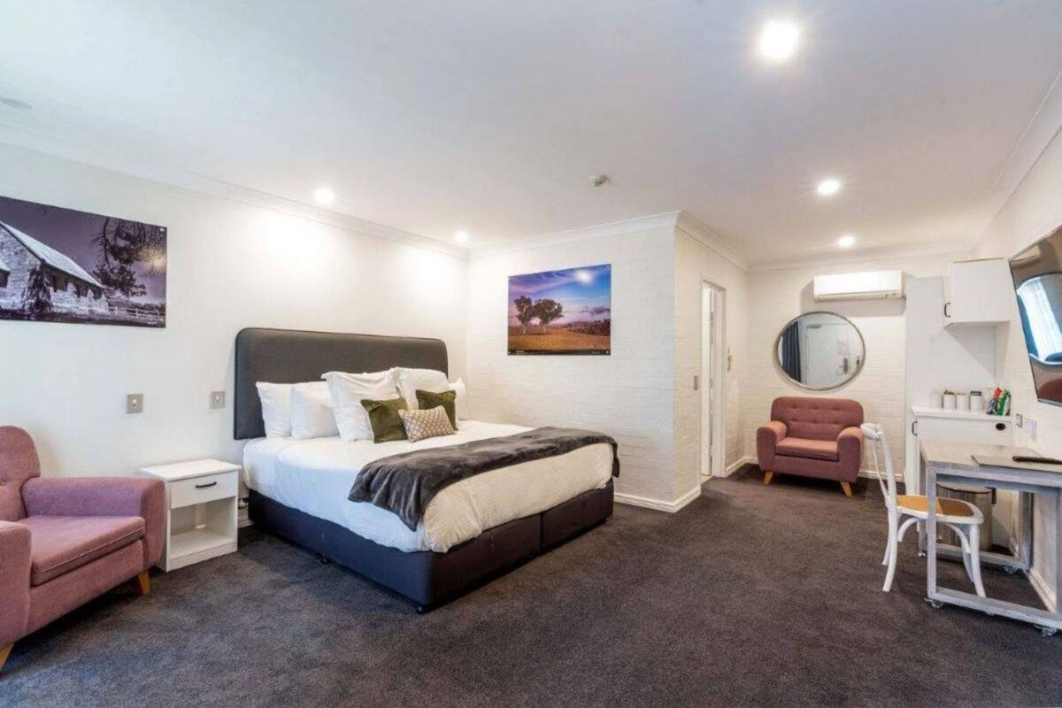 Un dormitorio con cama, escritorio, silla, sofá pequeño y dos televisores en la pared.