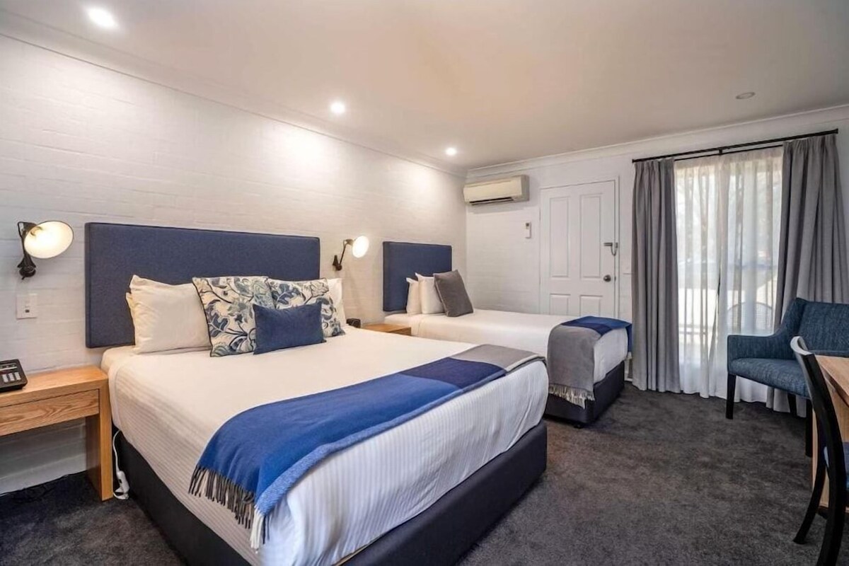Una habitación de hotel con dos camas, un escritorio, una silla y un ventanal con cortinas.