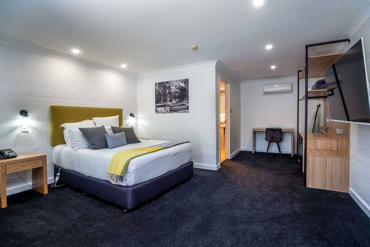 Una habitación de hotel moderna con una cama grande, mesitas de noche, un escritorio y un televisor.