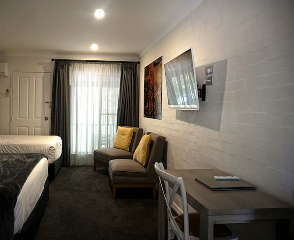 A hotel room with a bed, a desk, a chair, and a window with curtains.