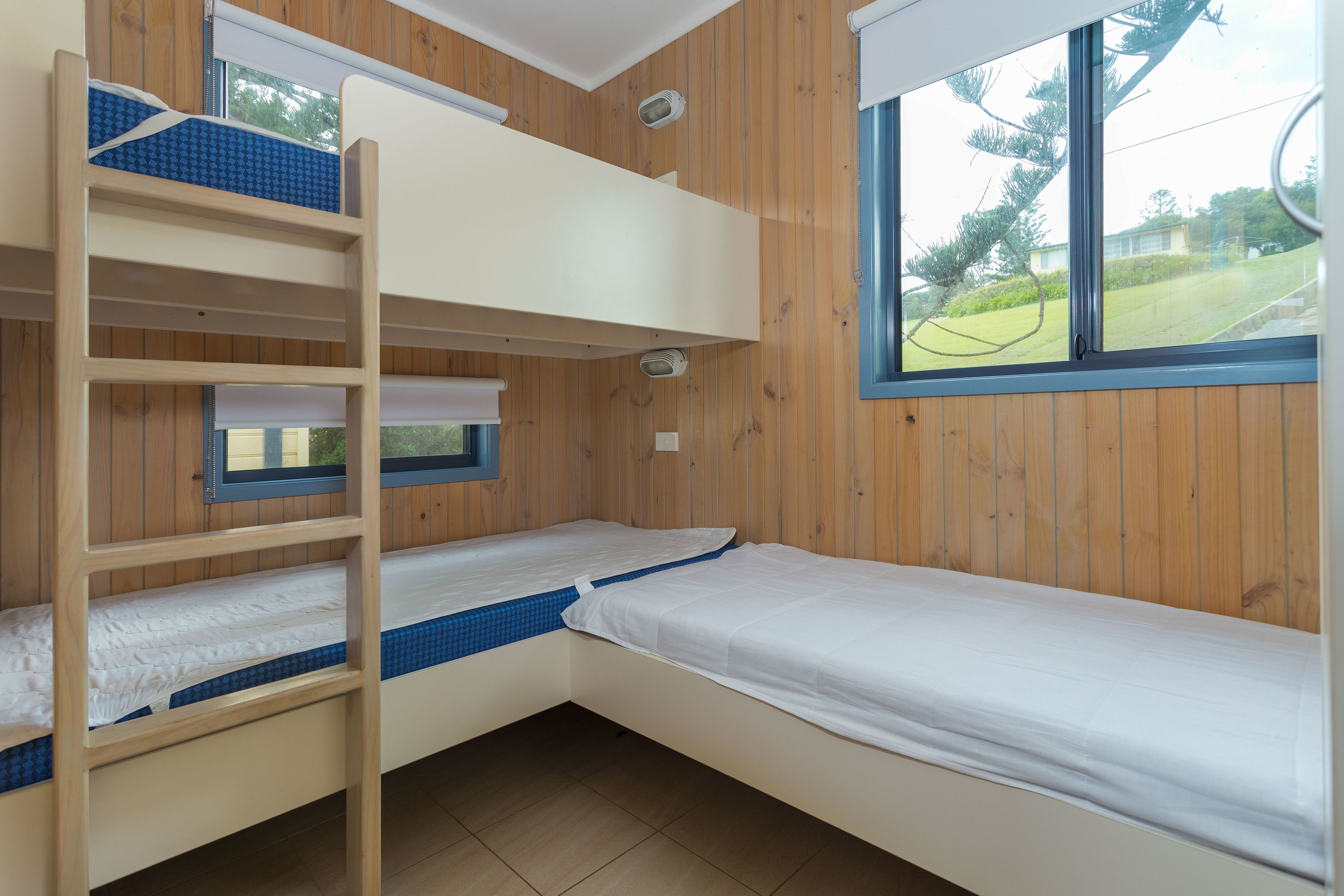 A bunk bed room with a window, wooden walls, and a view of greenery outside.