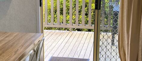 A room with a wooden table and chairs, a sliding glass door leading to a balcony with a white railing, and a view of the sea.