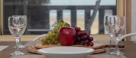 A table with a plate of fruit, two empty wine glasses, and a wooden board.