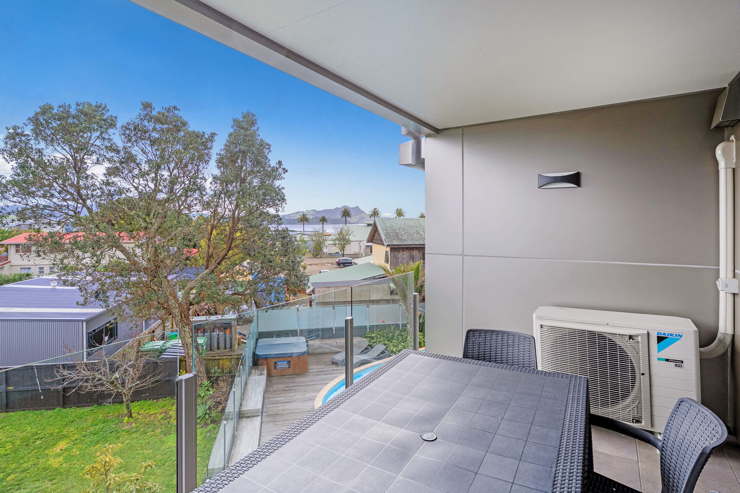 A balcony with a table and chairs, overlooking a pool and a garden.