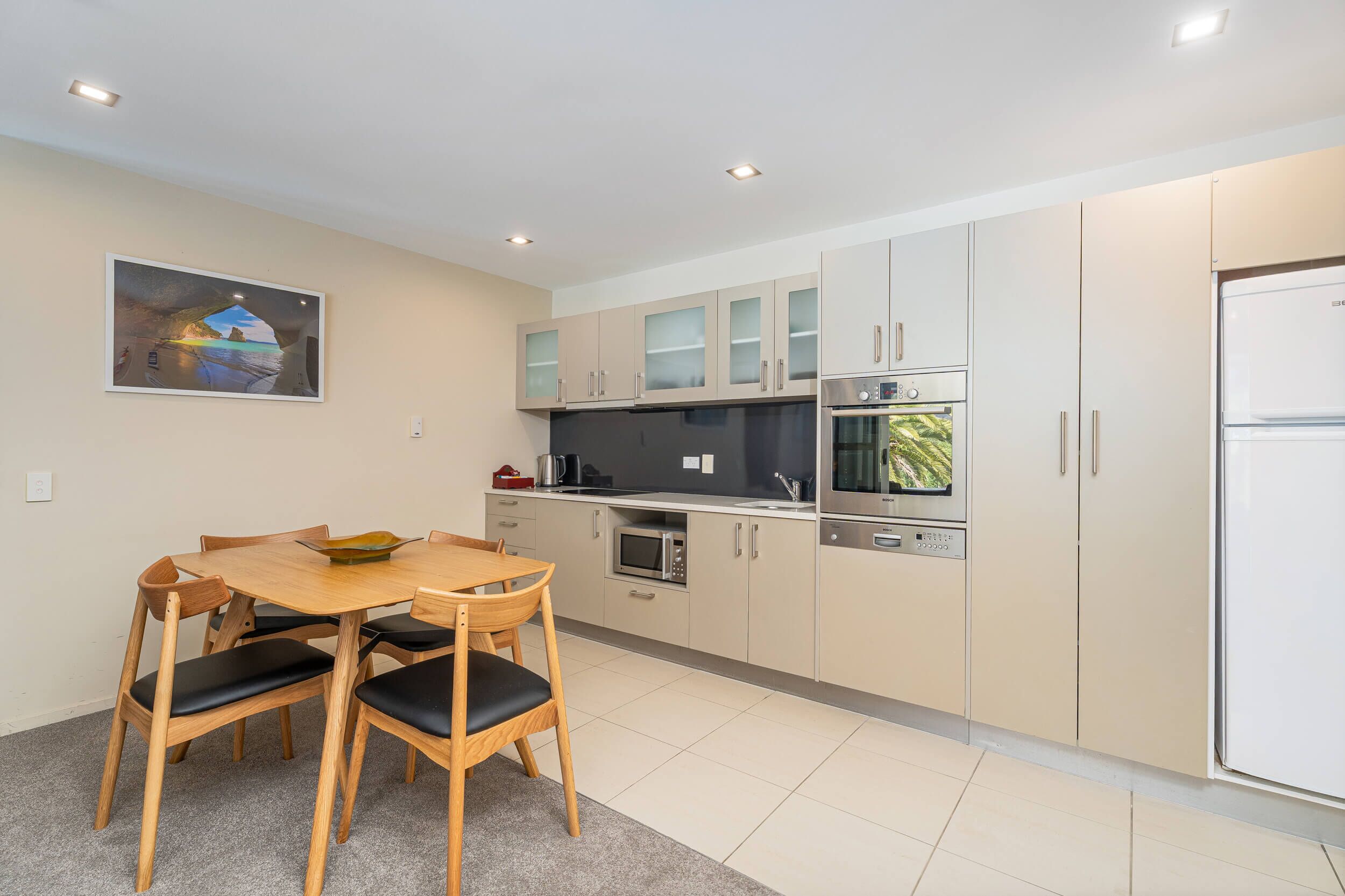 A modern kitchen with a dining table and chairs, a refrigerator, oven, microwave, and cabinets.