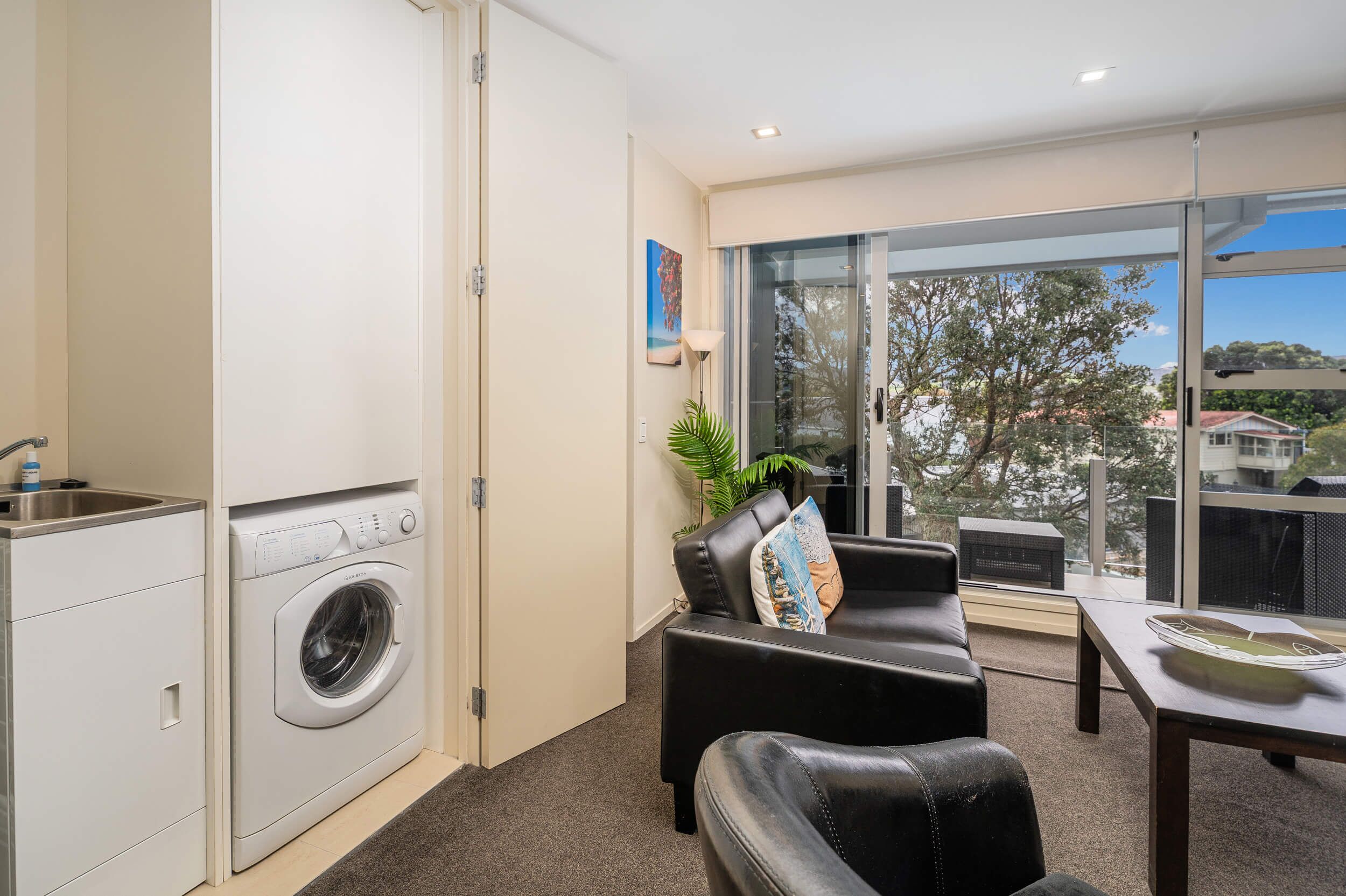 A modern apartment with a washing machine, a seating area with a view of the outdoors, and a dining table.