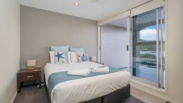 A modern bedroom with a large bed, a nightstand, a lamp, and a sliding glass door leading to a balcony.