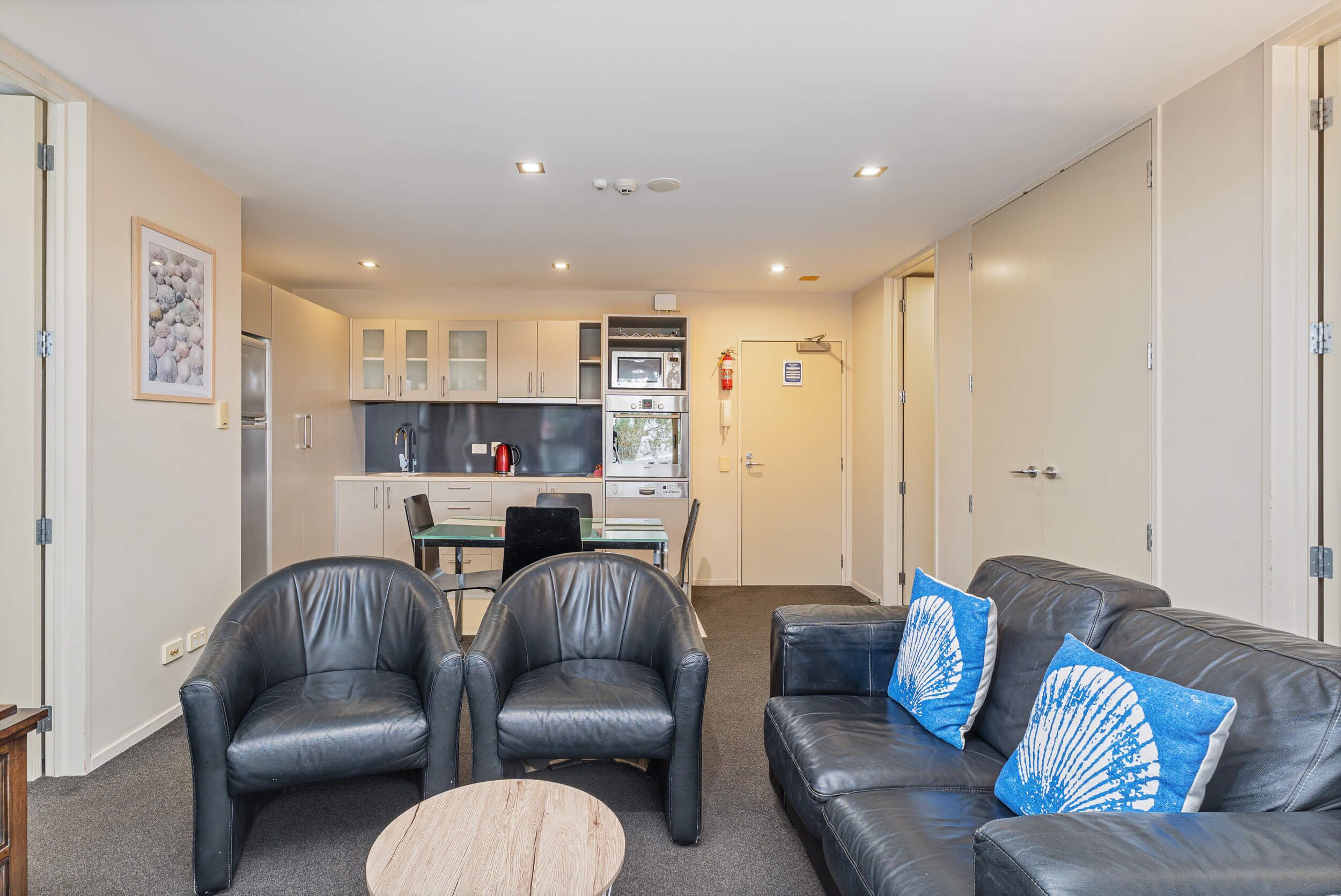 A modern living room with leather furniture, a dining area, and a kitchenette.