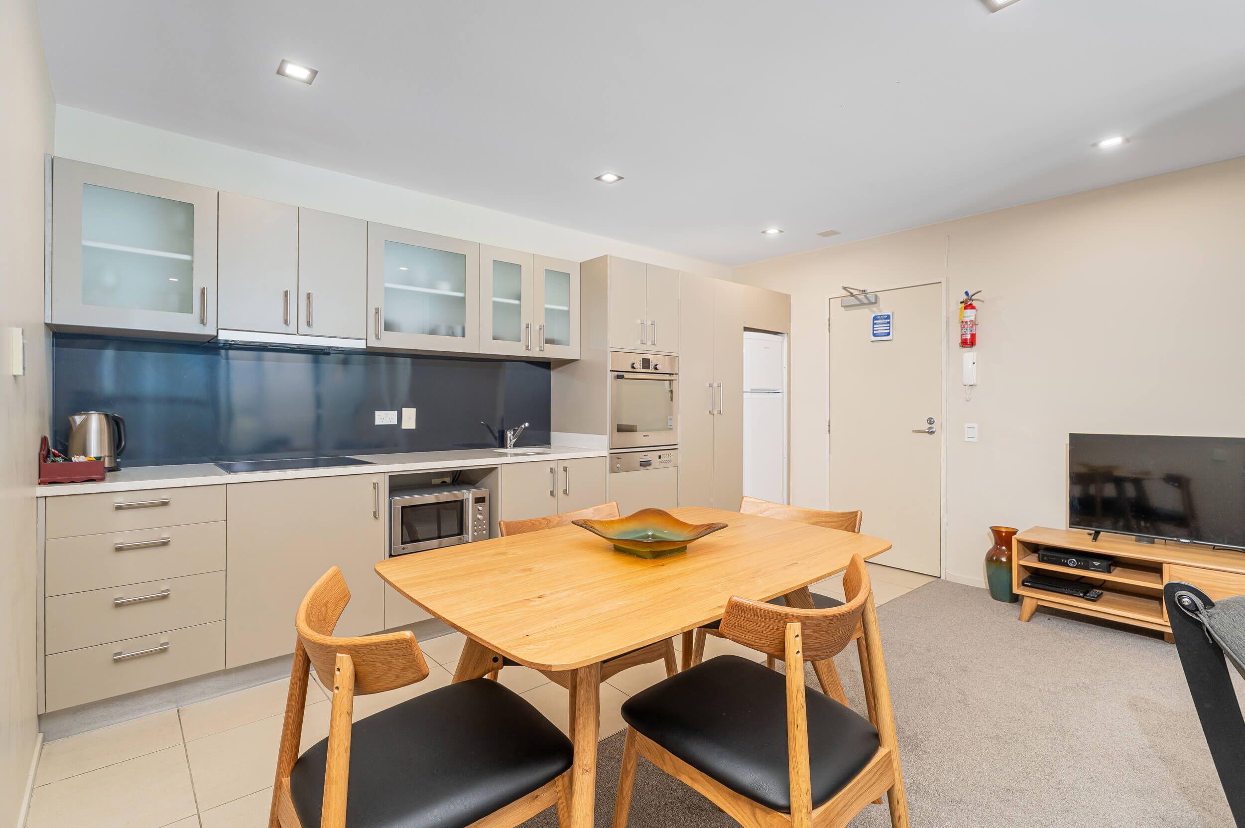 A modern kitchen with a dining area, including cabinets, a microwave, and a TV.