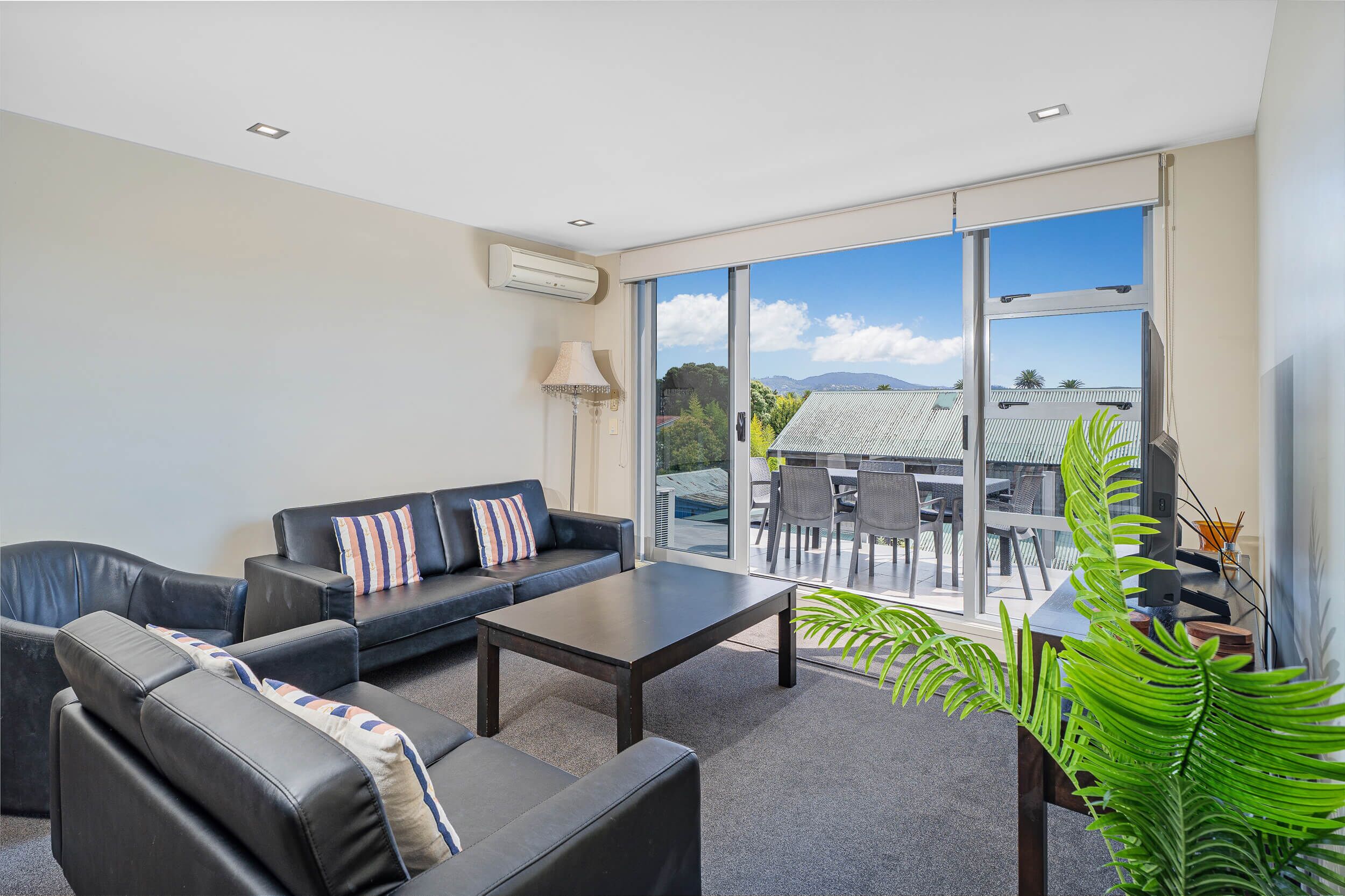 A modern living room with a sofa, coffee table, and a view of a balcony with outdoor furniture.
