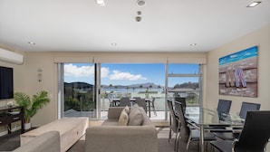 Una sala de estar moderna con una mesa de comedor de vidrio, asientos cómodos, un televisor y vistas al exterior.