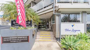 A building with a sign for 'Blue Lagoon' bar and eatery, and a sign for 'Vacancy' with a phone number. There are 1, 2, and 3 bedroom apartments available, with amenities like pool, spa, 50+ channels, lifts, and secure parking.