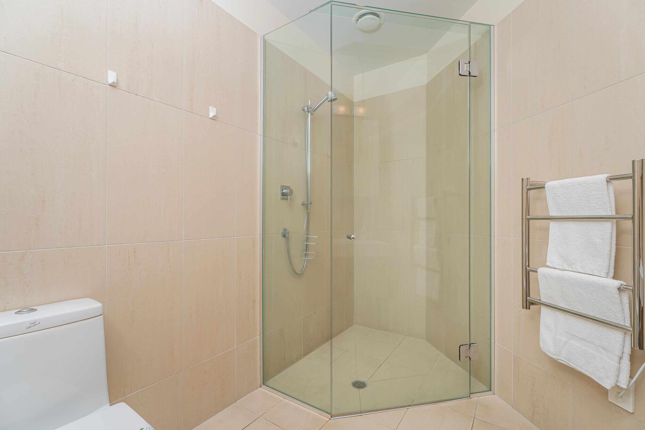 A glass-enclosed shower with a glass door, a white towel rack with multiple towels, and a toilet with a white lid.