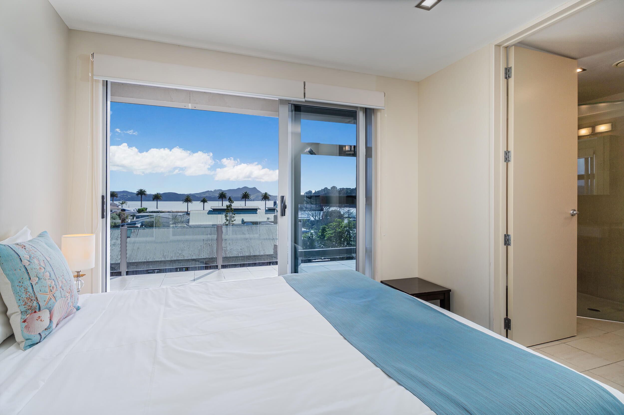 Quarto de hotel moderno com uma cama grande, vista para a cidade e varanda com guarda-corpo.