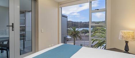 A hotel room with a large bed, a view of the beach, and a sliding door to the balcony.
