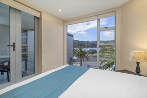 A hotel room with a large bed, a view of the beach, and a sliding door to the balcony. - Esplanade Apartments (Whitianga)