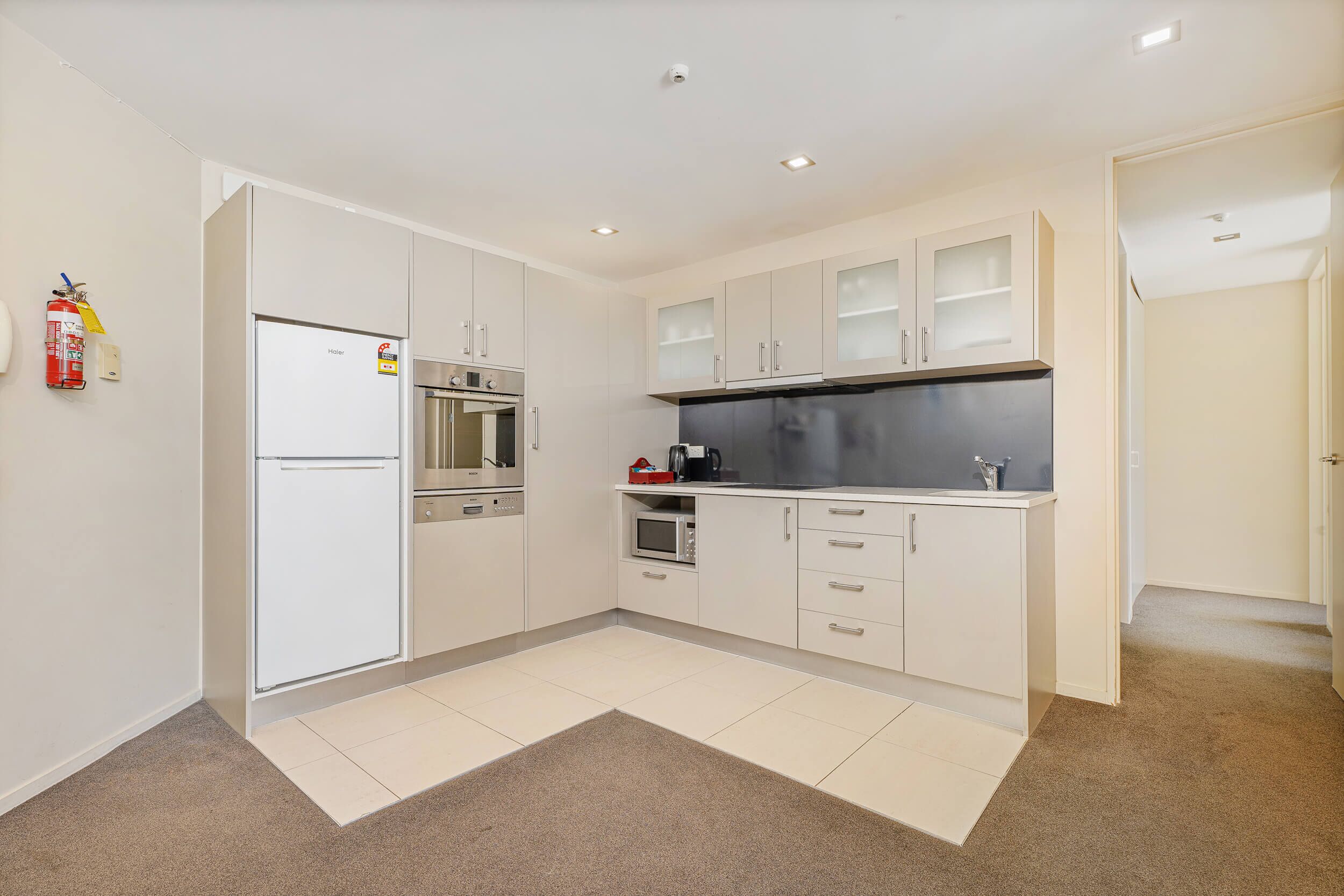 A modern kitchen with white cabinets, a stainless steel refrigerator, an oven, a microwave, and a coffee maker.