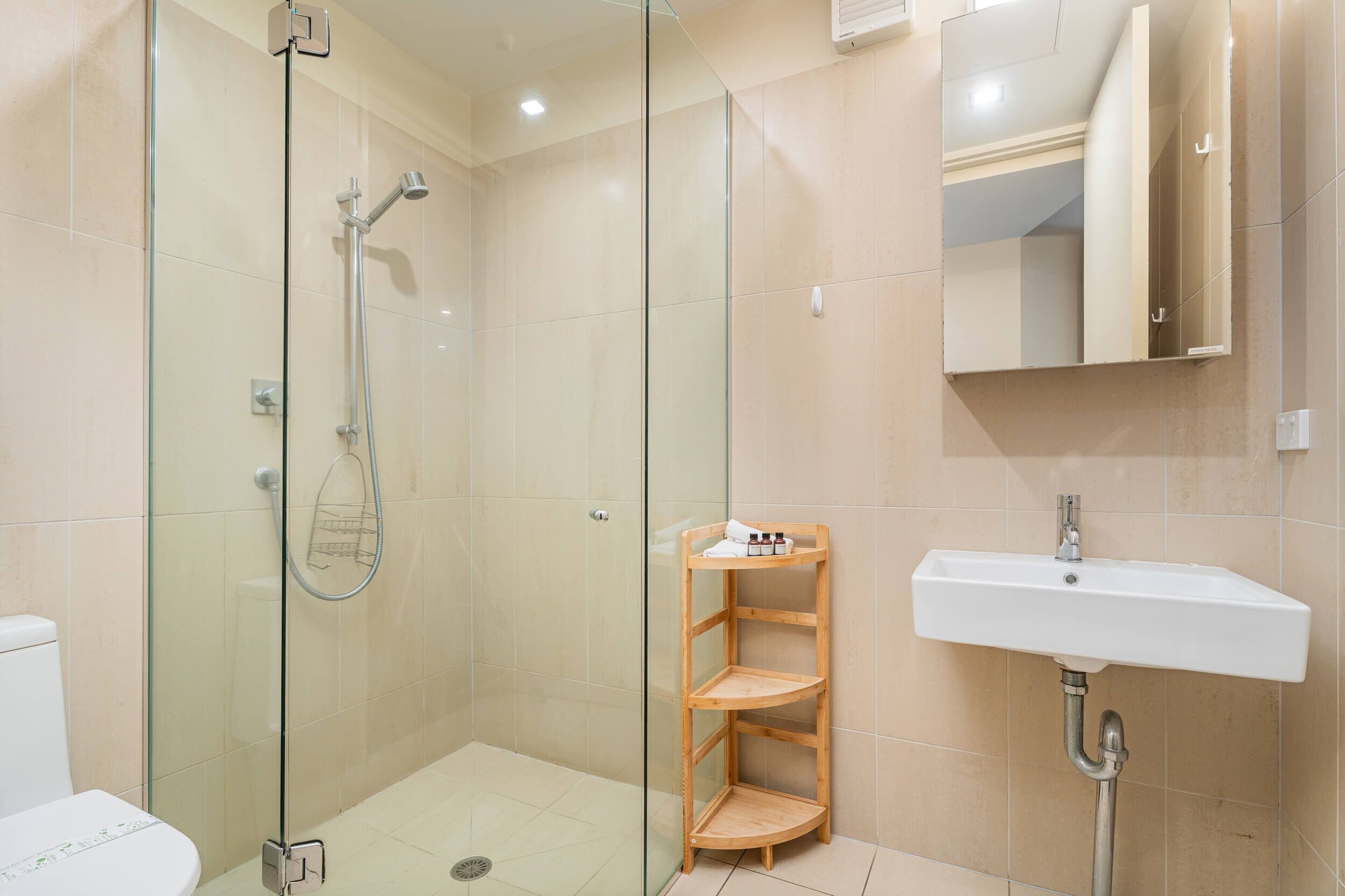 A modern bathroom with a glass-enclosed shower, a white sink, and a wooden shelf unit.