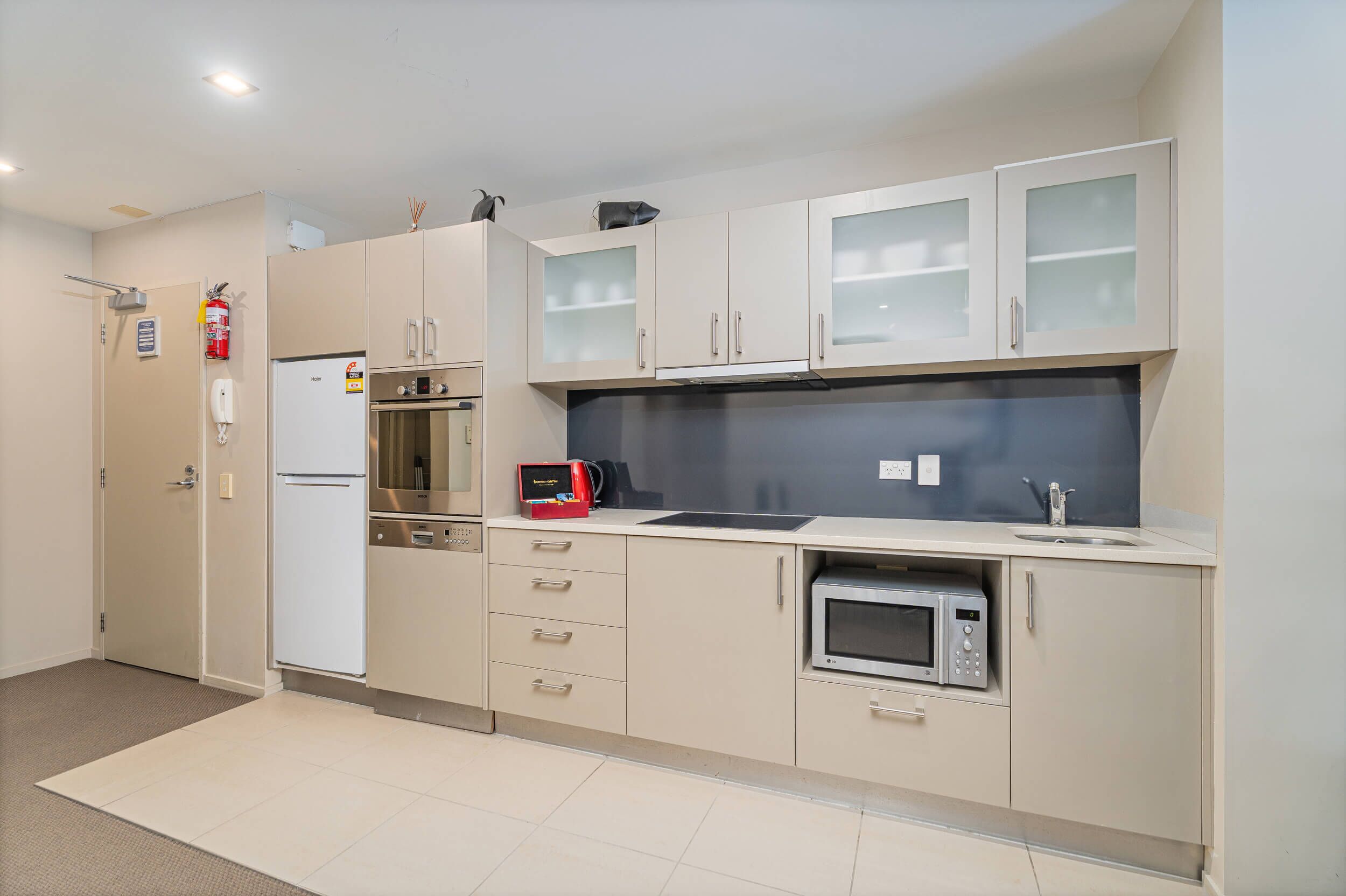 A modern kitchen with beige cabinets, a microwave, a stove, and a refrigerator.