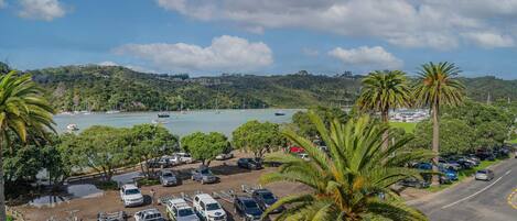 A coastal parking area with vehicles, a road, and a view of boats on the water.