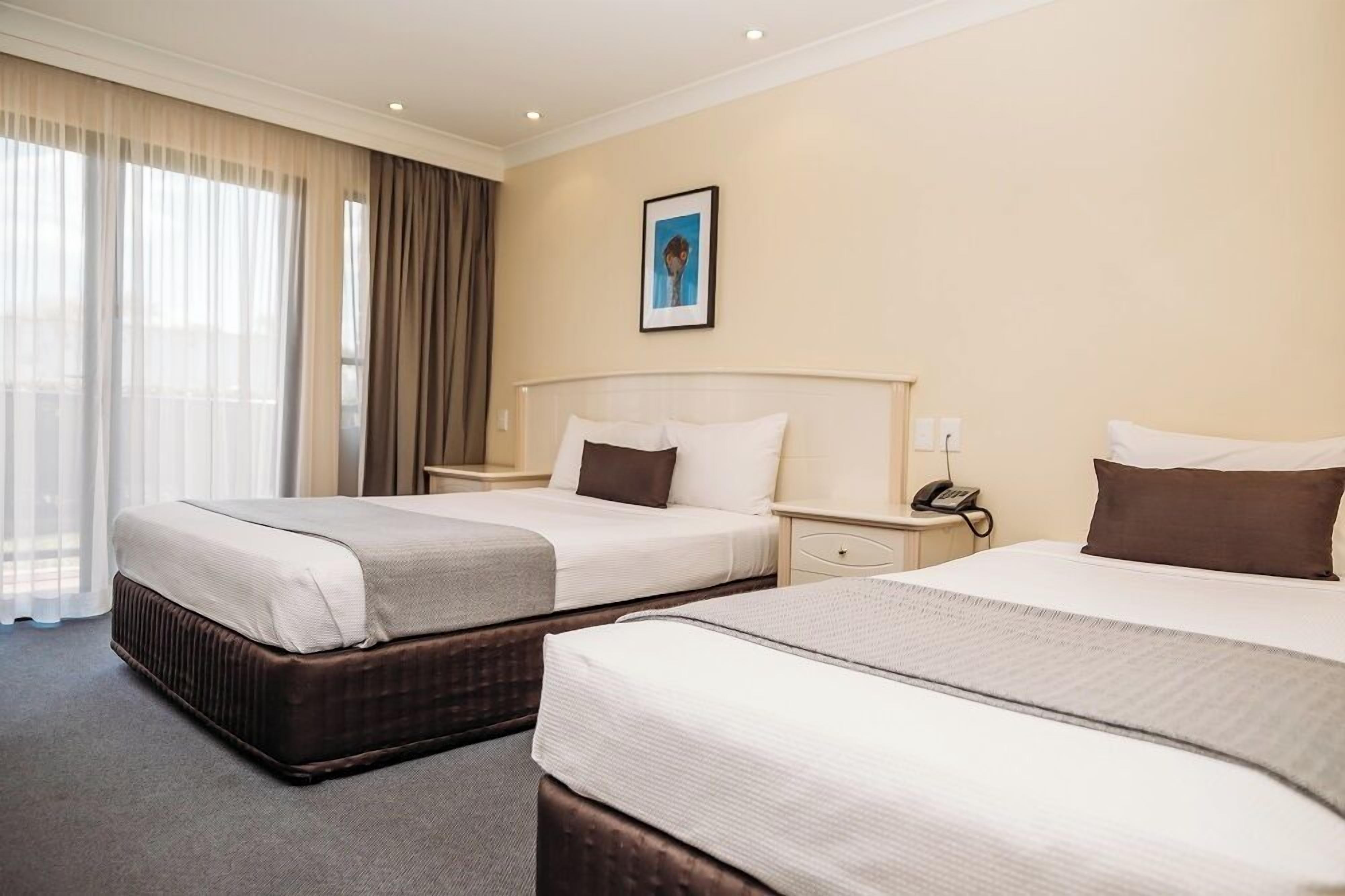 Une chambre d’hôtel avec deux lits, une table de chevet avec un téléphone et une fenêtre avec des rideaux.