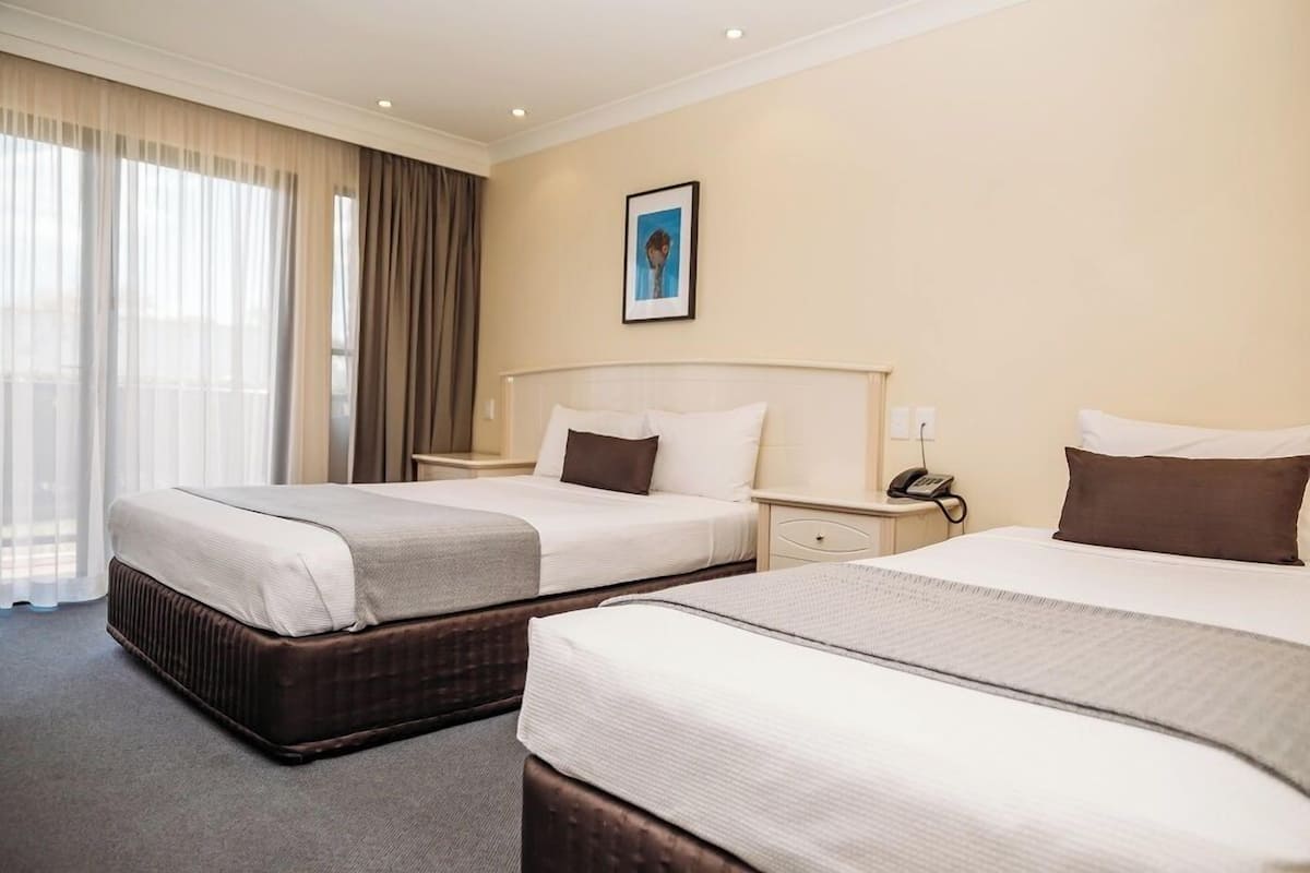 Une chambre d’hôtel avec deux lits, une table de chevet avec un téléphone et une fenêtre avec des rideaux.