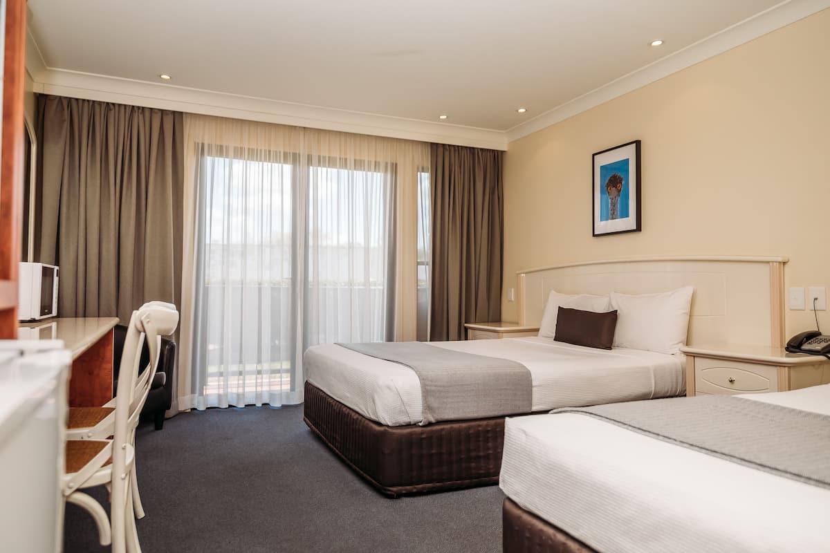 Une chambre d’hôtel avec deux lits, un bureau, une chaise et une fenêtre avec des rideaux.