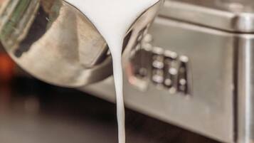 Una taza blanca de café con leche siendo servida desde una jarra de metal.