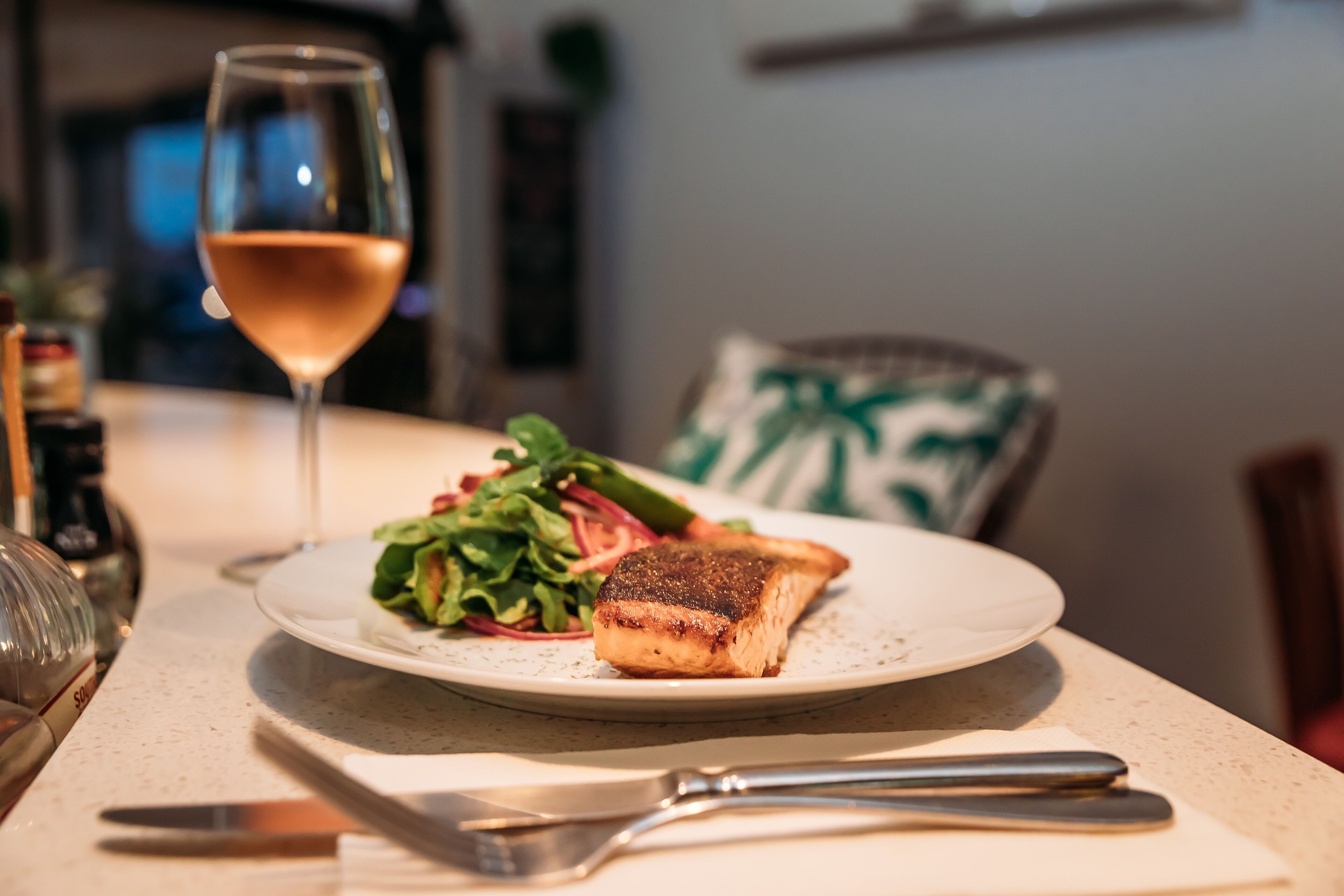 A plate with salmon and salad, a glass of wine, and cutlery on a table.