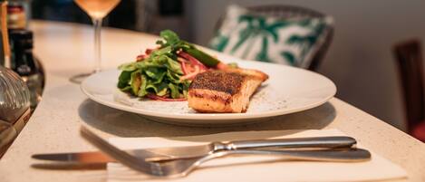A plate with salmon and salad, a glass of wine, and cutlery on a table.