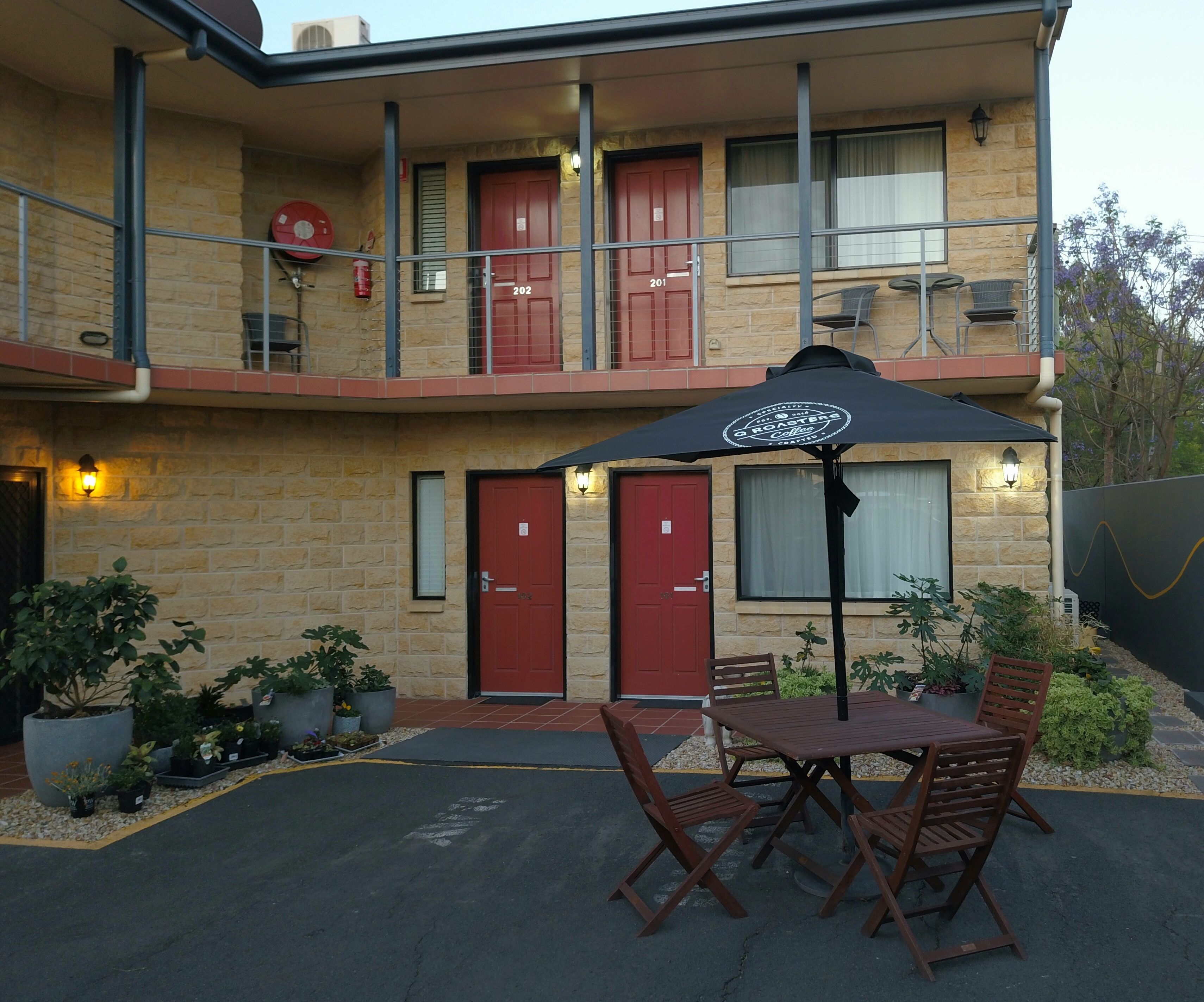 A two-story building with numbered doors, outdoor seating, and potted plants.