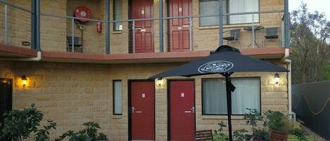 A two-story building with numbered doors, outdoor seating, and potted plants.
